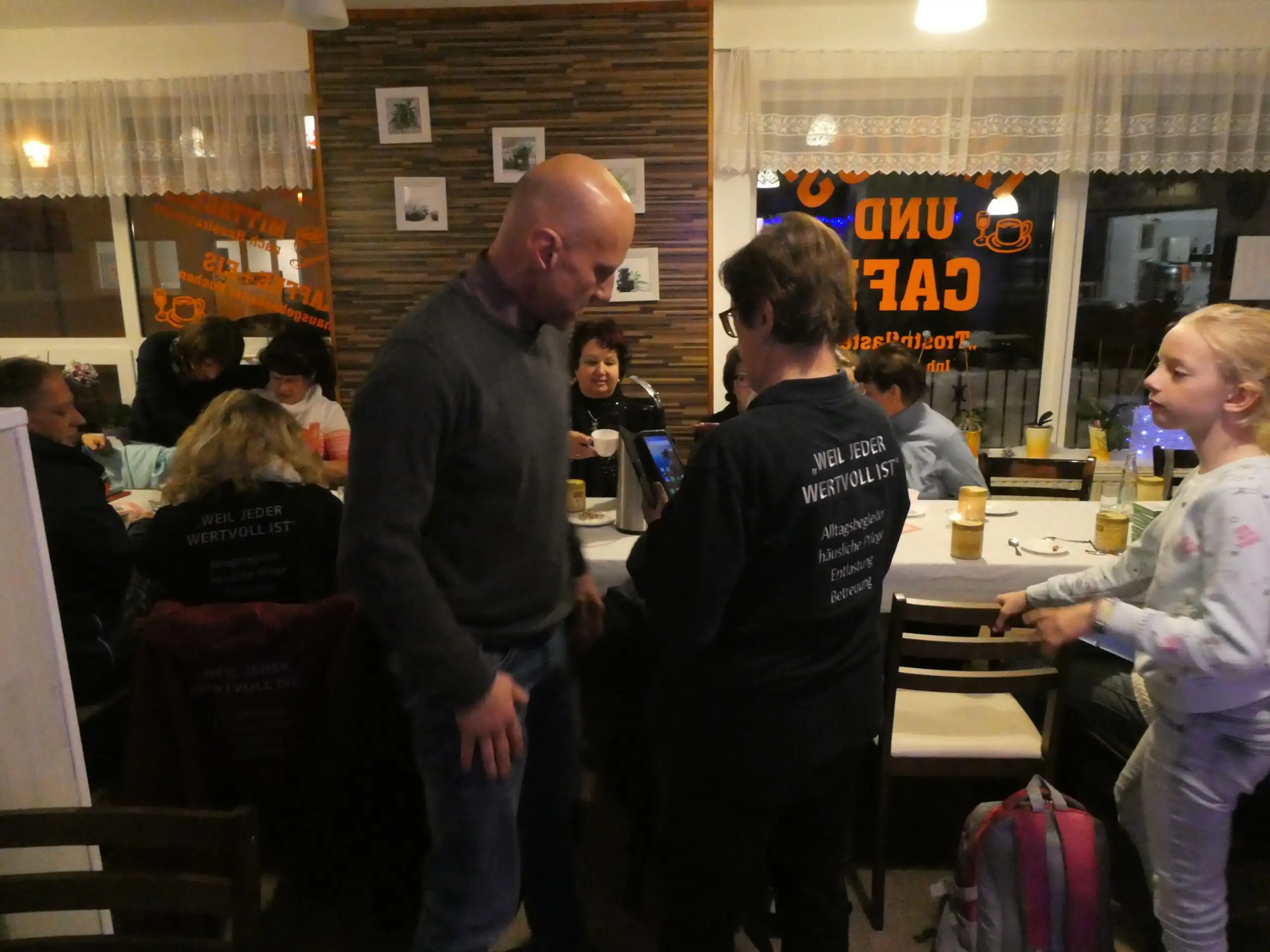 Ein Pflegeteam trifft sich bei einem Gemeinschaftscafe mit Besuchern und Angehörigen. Die Szene zeigt eine informelle Begegnung in einem belebten Innenraum.
