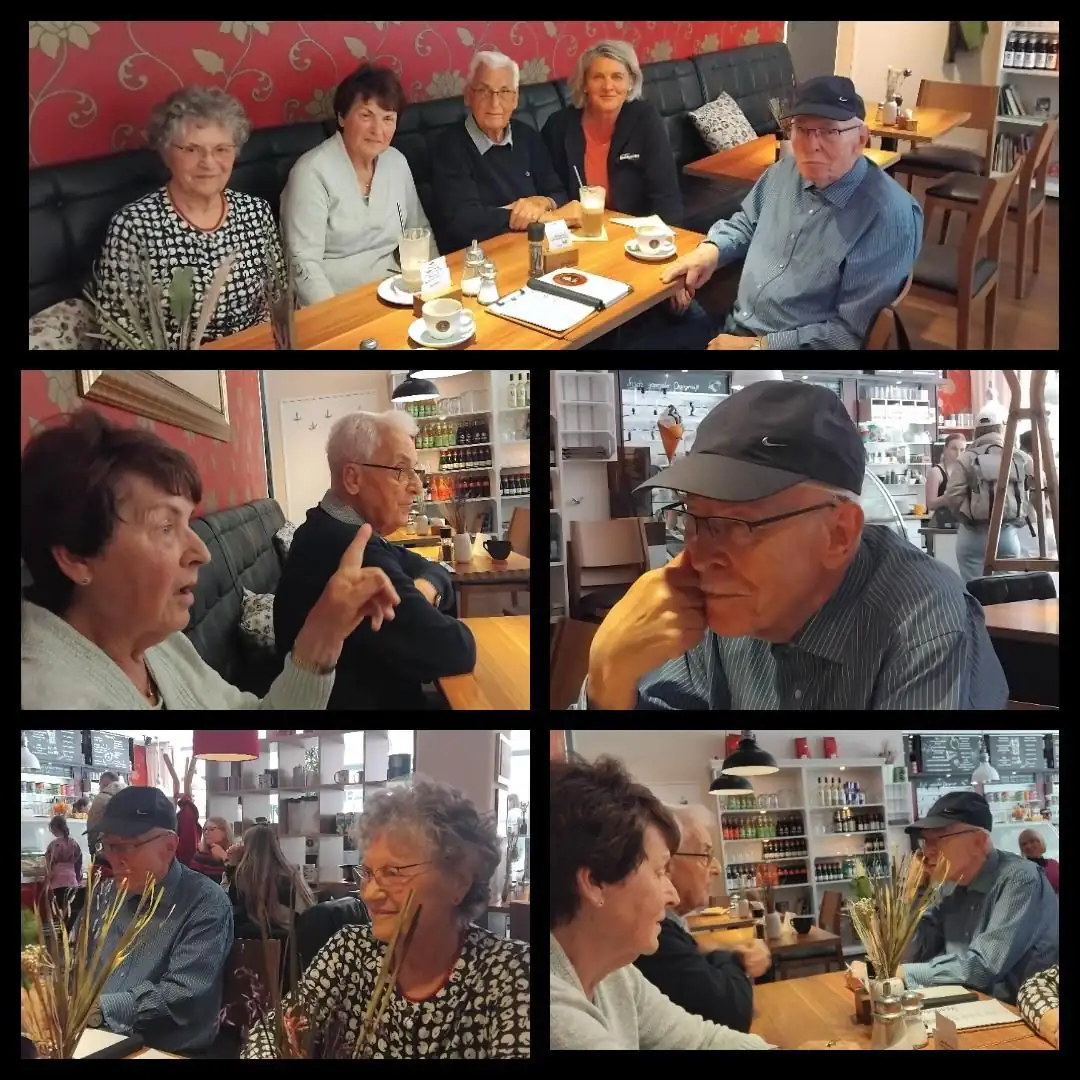 Eine Gruppe älterer Menschen sitzt in einem Café zusammen und unterhält sich bei Getränken. Die Szene zeigt ein geselliges Beisammensein im Alltag.