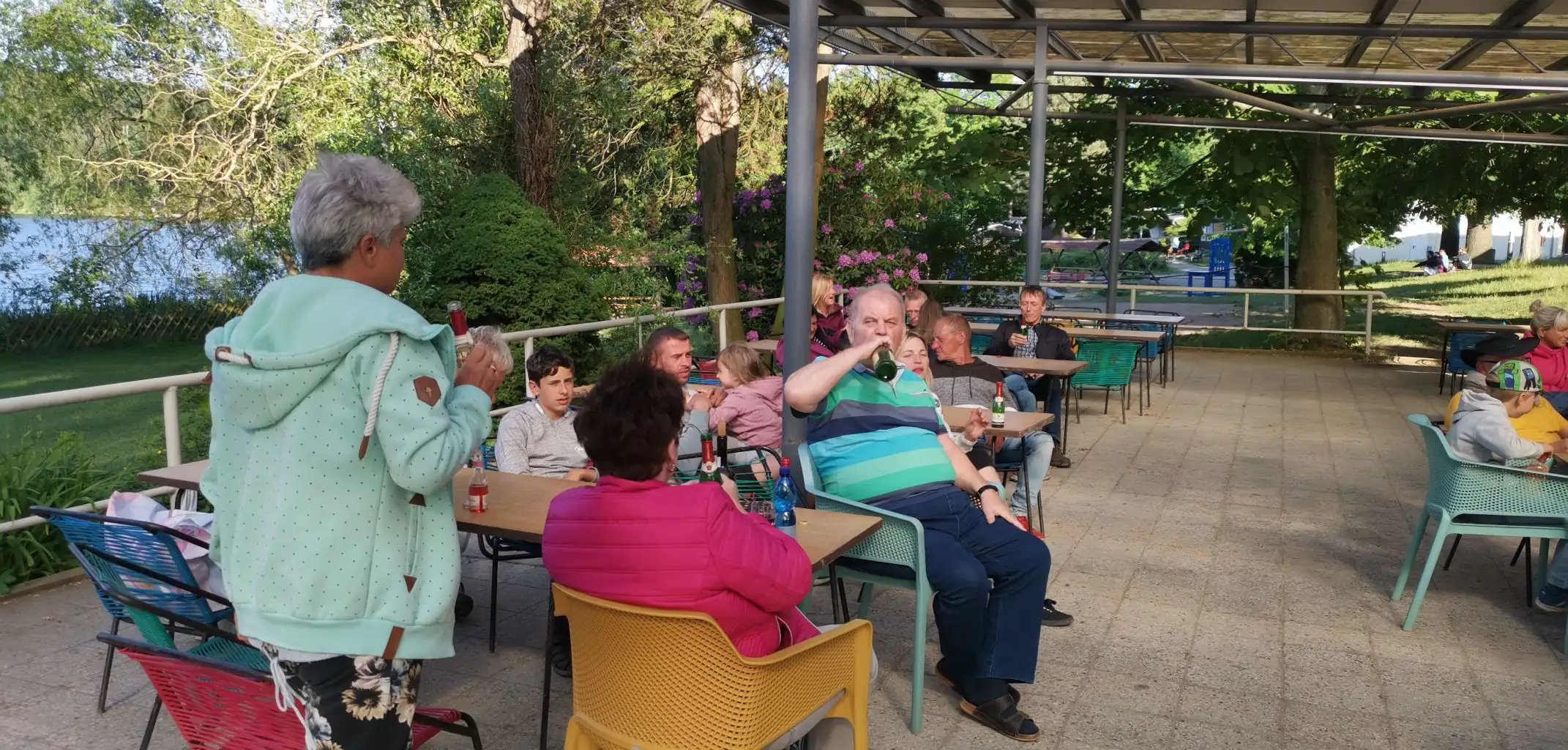 Eine Gruppe von Menschen sitzt an Tischen im Freien unter einer Überdachung und genießt die Zeit zusammen.