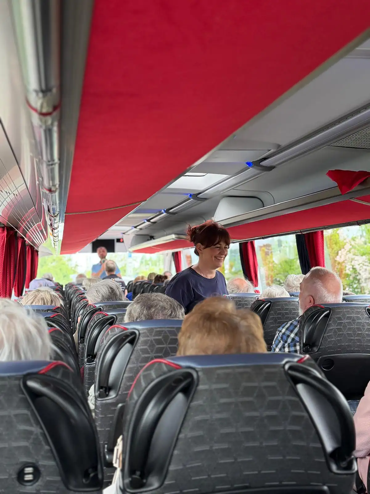 Senioren bei einer gemeinsamen Busausfahrt mit einer Betreuerin im Gang. Die Szene zeigt soziale Aktivität und Mobilität im Pflegekontext.