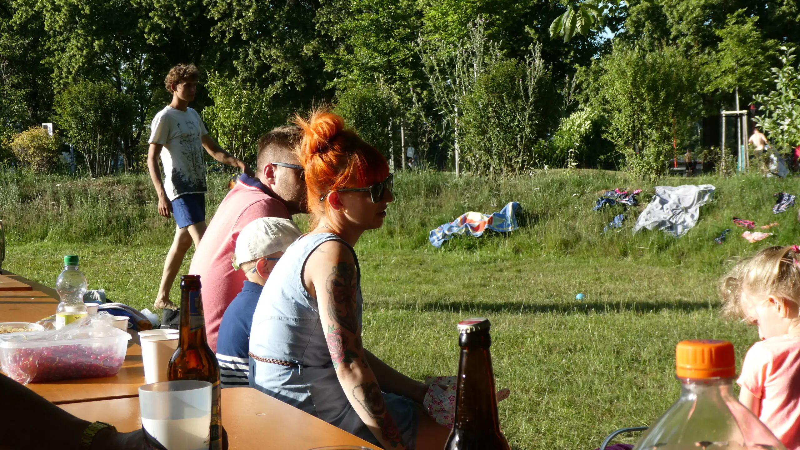 Eine Gruppe von Menschen sitzt an einem Picknicktisch im Park, auf dem diverse Getränkeflaschen stehen.